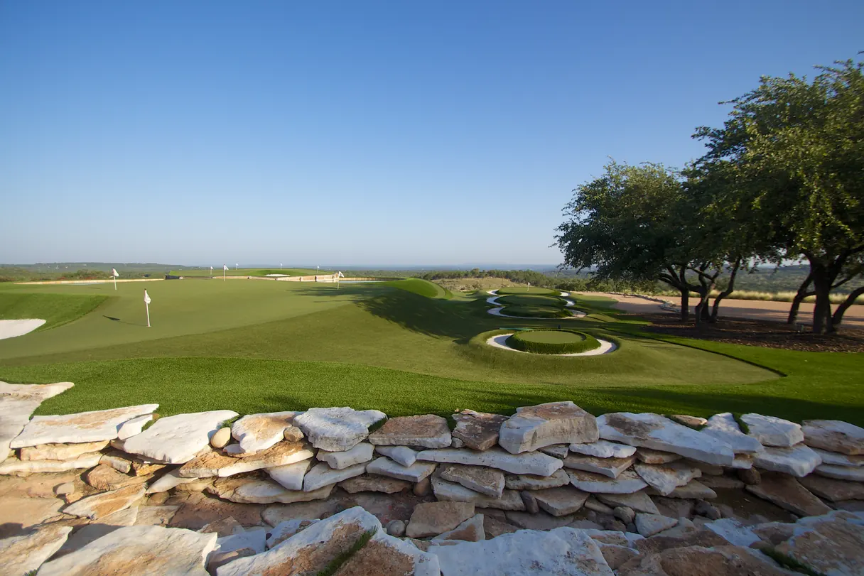Backyard putting green with a stone retaining wall and open sky