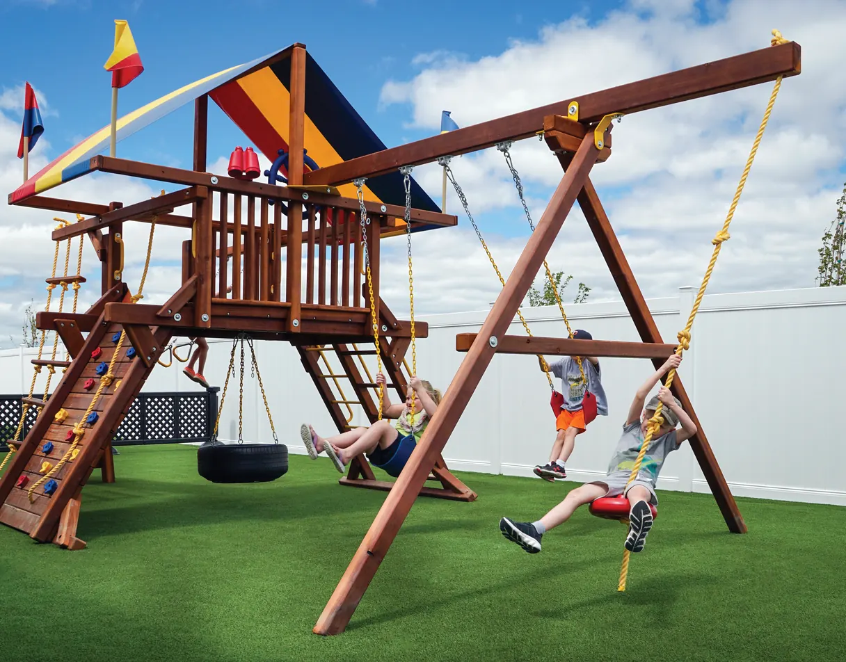 Children playing on a wooden swing set installed over SYNLawn artificial turf