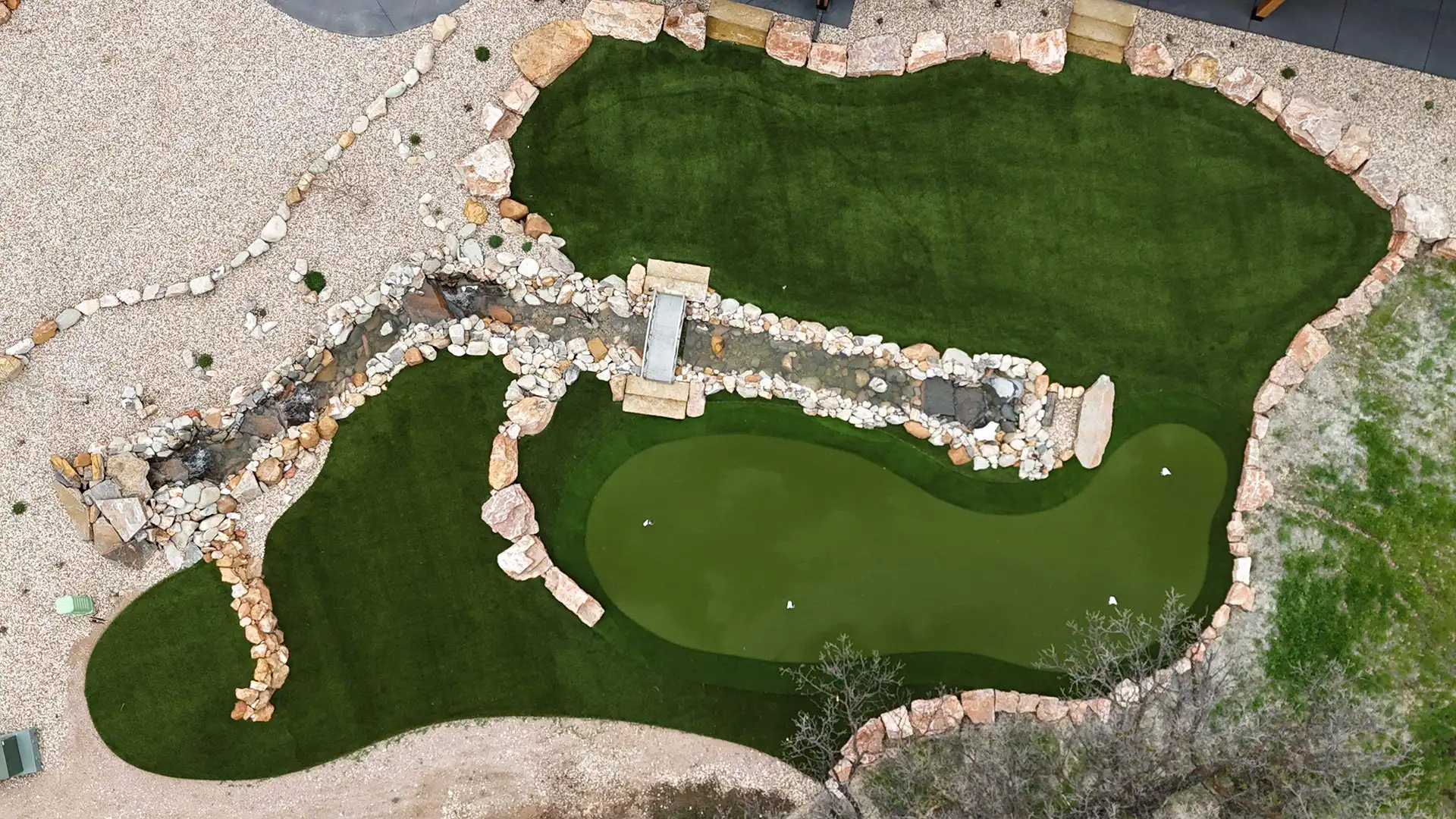 Backyard putting green with five flagsticks, sand bunker, and basketball hoop on artificial turf